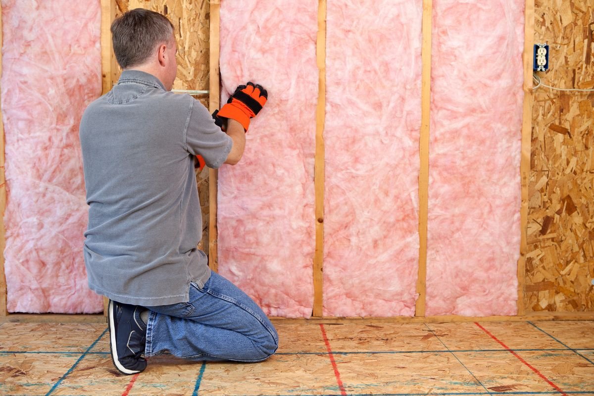 A man is engaged in installing pink insulation in a room, representing a professional insulation installation service.