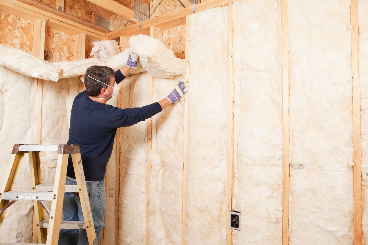 A man installs insulation in a room, demonstrating the process for an insulation installation service.