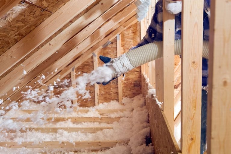 A man operates a vacuum to extract insulation from a home during an insulation installation service.