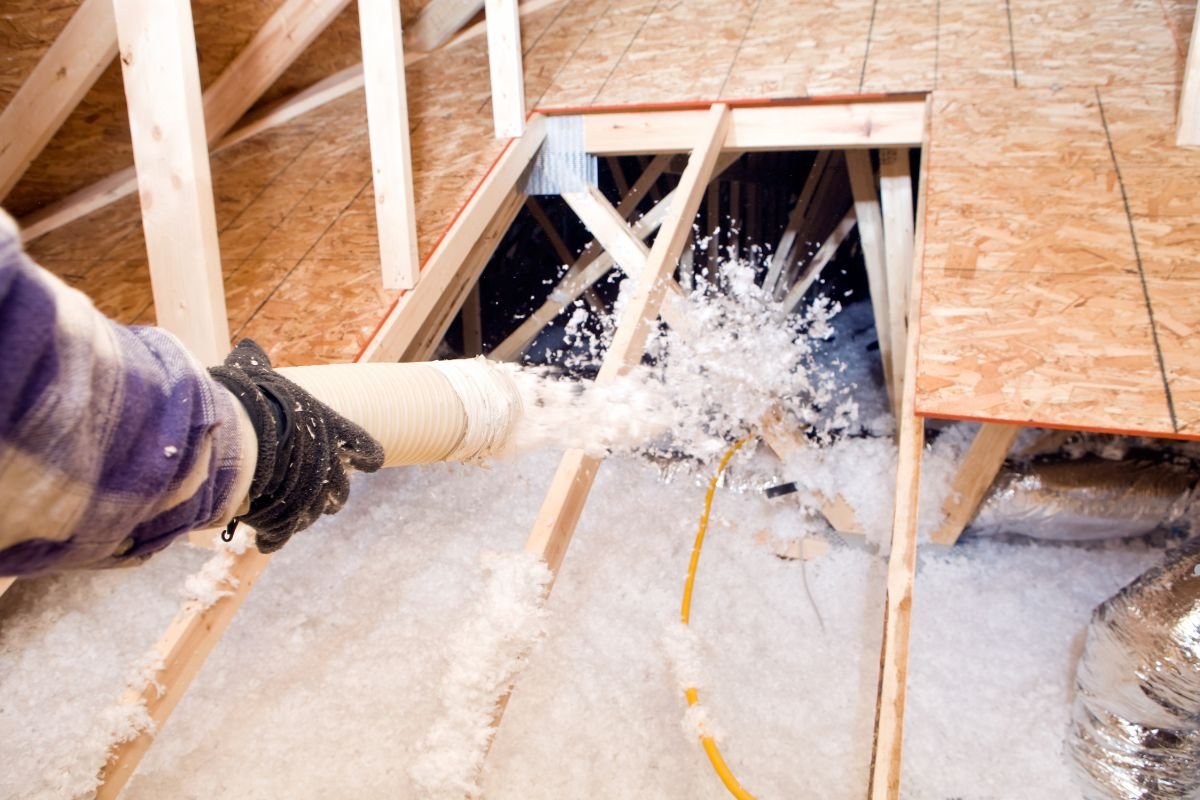 A person operates a vacuum to remove cellulose insulation during an installation service.